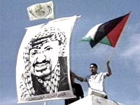 Fotografa Un palestino se manifiesta en lo alto de un edificio con un cartel de Yasir Arafat